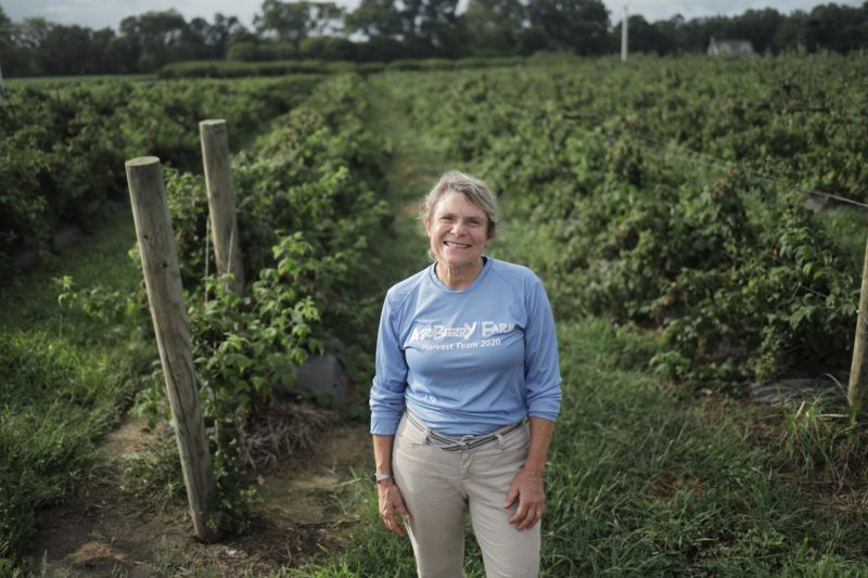 Anne Geyer standing in her berry field with rows of trellised berries on either side of her. 