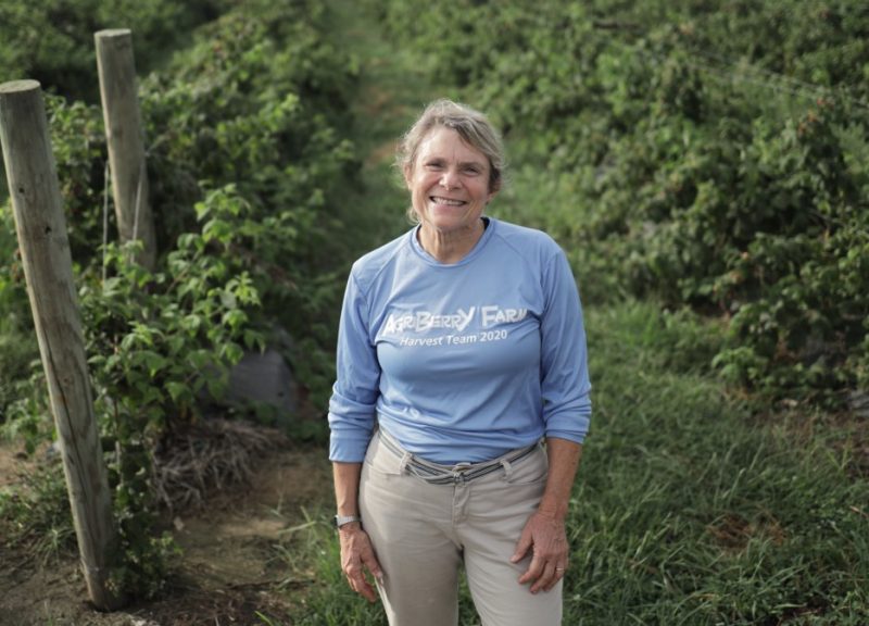 Anne Geyer standing in her berry field with rows of trellised berries on either side of her. 